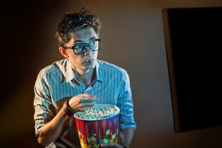 A man watches the movie alone in the glasses and eats popcornの写真素材