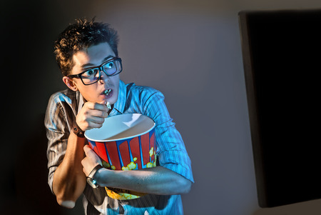 A man watches the movie alone in the glasses and eats popcornの写真素材