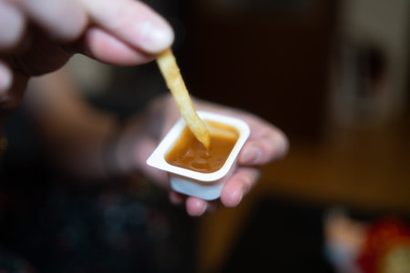 Close up of a woman's hand holding a french fry in a bowl