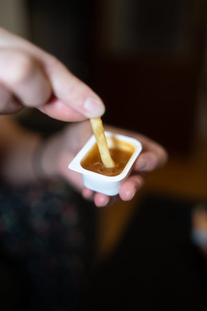 Close up of a woman's hand dipping french fries in a bowl