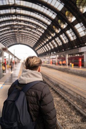 Young man waiting for the train at the platform of a railway station