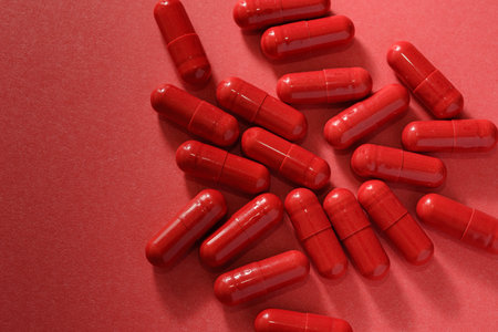 Red capsules or pills scattered on red background