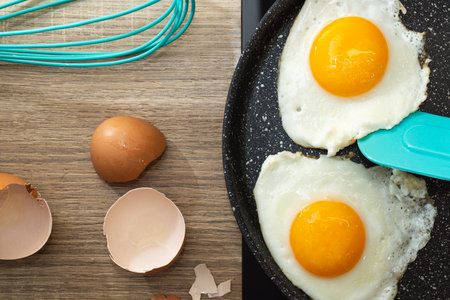 Flat lay of fried eggs in frying pan, spatula and eggshell.の写真素材