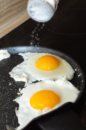 Salting of fried eggs in a frying pan on electric stove portrait view.の写真素材