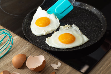 turn over of fried eggs with spatula in a frying pan and eggshell on the table.の写真素材