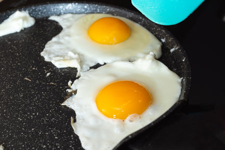 Fried eggs and kitchen spatula in a frying pan on electric stove.の写真素材