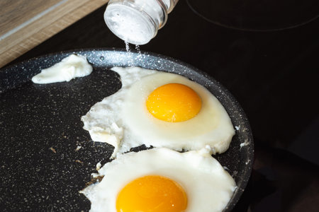 Salting of fried eggs in a frying pan on electric stove landscape view.の写真素材