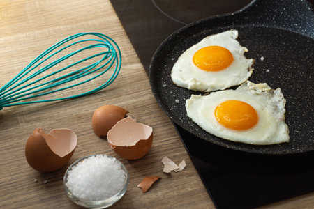 fried eggs in a frying pan, salt and eggshell on the table.の写真素材