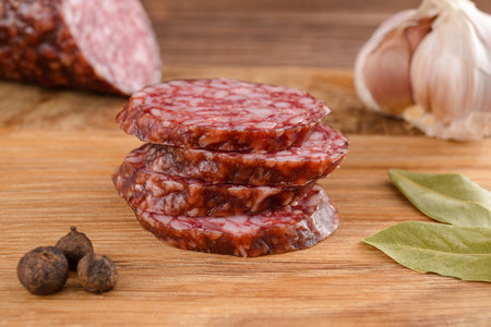 Salami sausage cut slices with garlic, bay leaf and pepper on cutting boardの写真素材