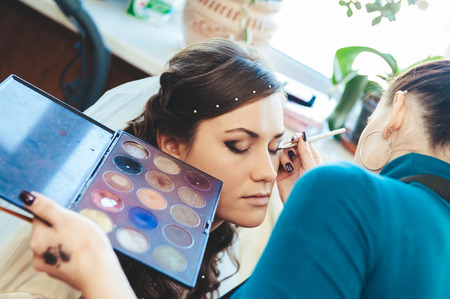 Woman applying make up for a bride in her wedding day near mirror. Closeup of a makeup artist applying makeupの写真素材
