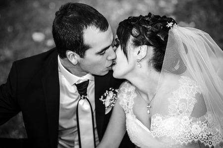 Young couple kissing in wedding gown. Bride holding bouquet of flowers.の写真素材