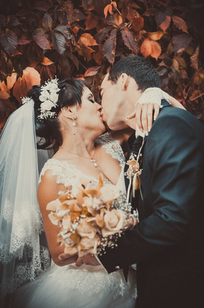 Young couple kissing in wedding gown. Bride holding bouquet of flowers.の写真素材