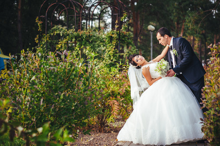 Young couple kissing in wedding gown. Bride holding bouquet of flowers.の写真素材