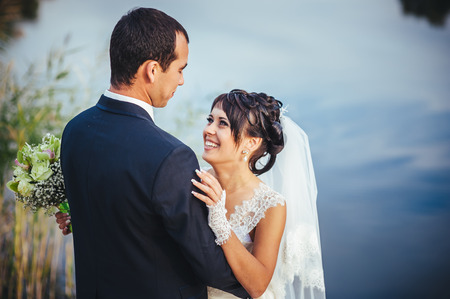 wedding: bride and groom on the seashore. Honeymoon. The bride and groom hugging on the shore of Lake. groom and bride hugging on a green lake. Groom and Bride in a park. wedding dress. Bridal wedding bouquet of flowersの写真素材