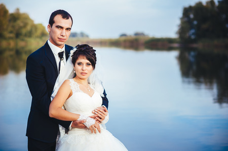 wedding: bride and groom on the seashore. Honeymoon. The bride and groom hugging on the shore of Lake. groom and bride hugging on a green lake. Groom and Bride in a park. wedding dress. Bridal wedding bouquet of flowersの写真素材