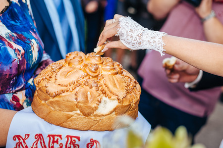 Groom holding slice of traditional wedding round loaf and bride salt itの写真素材
