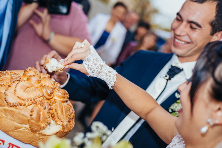 Groom holding slice of traditional wedding round loaf and bride salt itの写真素材
