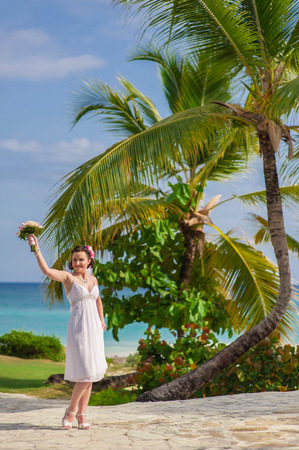 happy nice blonde bride walk near beach on green grass under palms.の写真素材