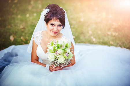 portrait of beautiful young bride holding bright bouquet of flowers in hands. wedding celebration. reception. nature green background. woman alone outdoors in park.の写真素材