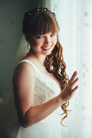 Young beautiful bride waits for groom near the window.の写真素材