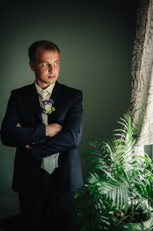Portrait of a handsome groom in classical interior. The man in the white shirt in the window dress cufflinksの写真素材