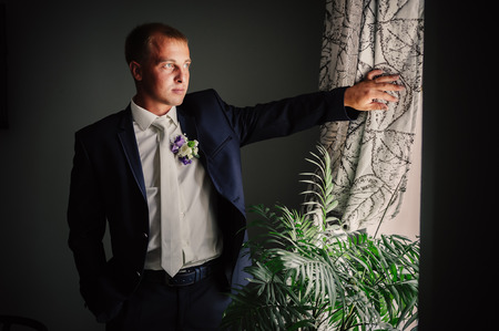 Portrait of a handsome groom in classical interior. The man in the white shirt in the window dress cufflinksの写真素材