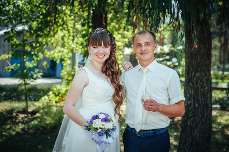 wedding couple kissing in green summer park. bride and groom kissing, standing together outdoors, hugging among green trees. Bride holding wedding bouquet of flowers.の写真素材