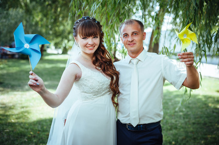 wedding couple kissing in green summer park. bride and groom kissing, standing together outdoors, hugging among green trees. Bride holding wedding bouquet of flowers.の写真素材