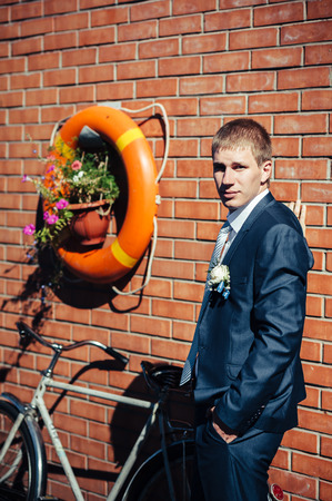 Happy young groom on their wedding day. Handsome groom thinking and putting on his bowtie while getting dressed for his wedding. Handsome caucasian man in tuxedoの写真素材
