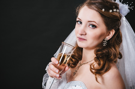 Fashion model with bridal bouquet and glass wearing wedding dress at black studio background.の写真素材