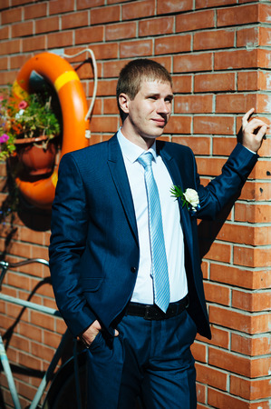 Happy young groom on their wedding day. Handsome groom thinking and putting on his bowtie while getting dressed for his wedding. Handsome caucasian man in tuxedoの写真素材