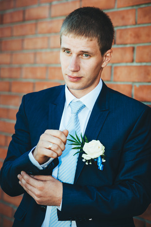 Happy young groom on their wedding day. Handsome groom thinking and putting on his bowtie while getting dressed for his wedding. Handsome caucasian man in tuxedoの写真素材