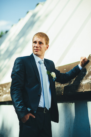 Happy young groom on their wedding day. Handsome groom thinking and putting on his bowtie while getting dressed for his wedding. Handsome caucasian man in tuxedoの写真素材