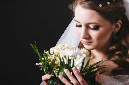 Fashion model with bridal bouquet and glass wearing wedding dress at black studio background.の写真素材