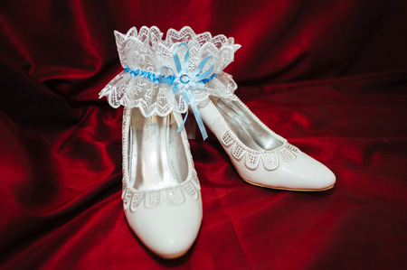 Luxury wedding shoes. Elegant bridal shoes and a white garter on red backgroundの写真素材