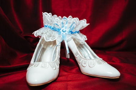 Luxury wedding shoes. Elegant bridal shoes and a white garter on red backgroundの写真素材
