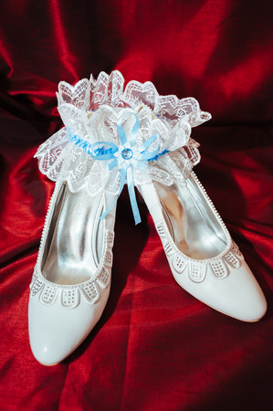 Luxury wedding shoes. Elegant bridal shoes and a white garter on red backgroundの写真素材