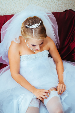 Garter on the leg of a bride, slim sexy bride in wedding luxury dress showing her silk garter with golden ribbon. woman have a final preparation for wedding ceremony. Wedding day moments.の写真素材
