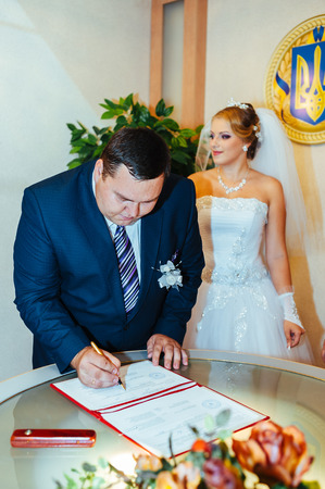 Wedding ceremony. Registry office. A newly-married couple signs the marriage document.Young couple signing wedding documents.の写真素材
