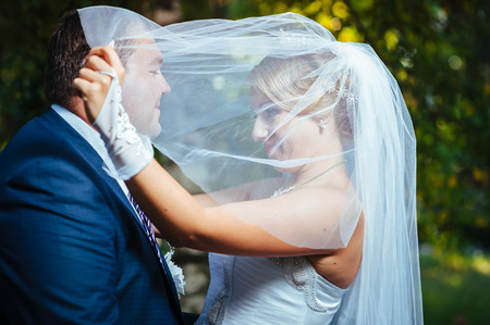 Bride And Groom Kissing Under Veil Holding Flower Bouquet In Handの写真素材