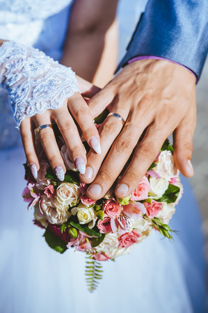 Hands of bride and groom with rings on wedding bouquetの写真素材
