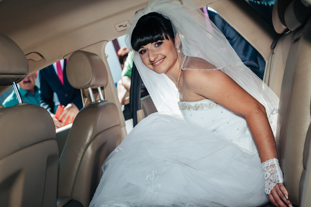 Happy bride sitting in limousine holding flower bouquet.の写真素材