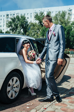 Happy groom helping his bride out of the wedding car.の写真素材