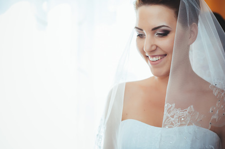 Bride getting ready. beautiful bride in white wedding dress with hairstyle and bright makeup. Happy sexy girl waiting for groom. Romantic lady in bridal dress have final preparation for wedding.の写真素材