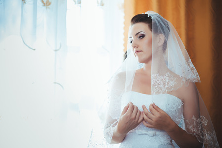 Bride getting ready. beautiful bride in white wedding dress with hairstyle and bright makeup. Happy sexy girl waiting for groom. Romantic lady in bridal dress have final preparation for wedding.の写真素材