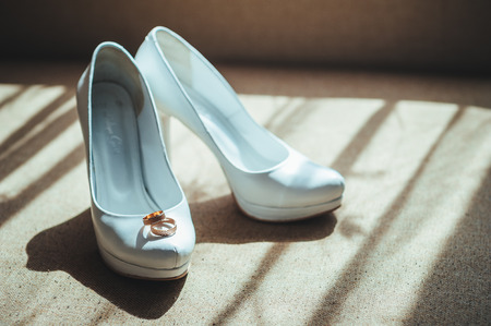 Two gold rings laying on white wedding bridal shoes.の写真素材