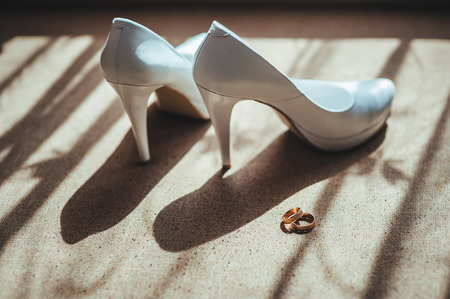 Two gold rings laying on white wedding bridal shoes.の写真素材