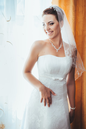 Bride getting ready. beautiful bride in white wedding dress with hairstyle and bright makeup. Happy sexy girl waiting for groom. Romantic lady in bridal dress have final preparation for wedding.の写真素材