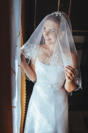 Bride getting ready. beautiful bride in white wedding dress with hairstyle and bright makeup. Happy sexy girl waiting for groom. Romantic lady in bridal dress have final preparation for wedding.の写真素材