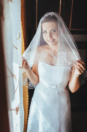 Bride getting ready. beautiful bride in white wedding dress with hairstyle and bright makeup. Happy sexy girl waiting for groom. Romantic lady in bridal dress have final preparation for wedding.の写真素材